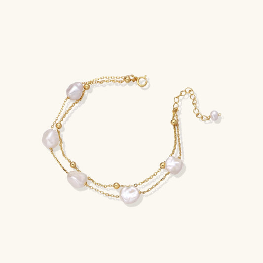 Double-strand gold bracelet with irregular baroque pearls and smooth freshwater pearls on cream background.