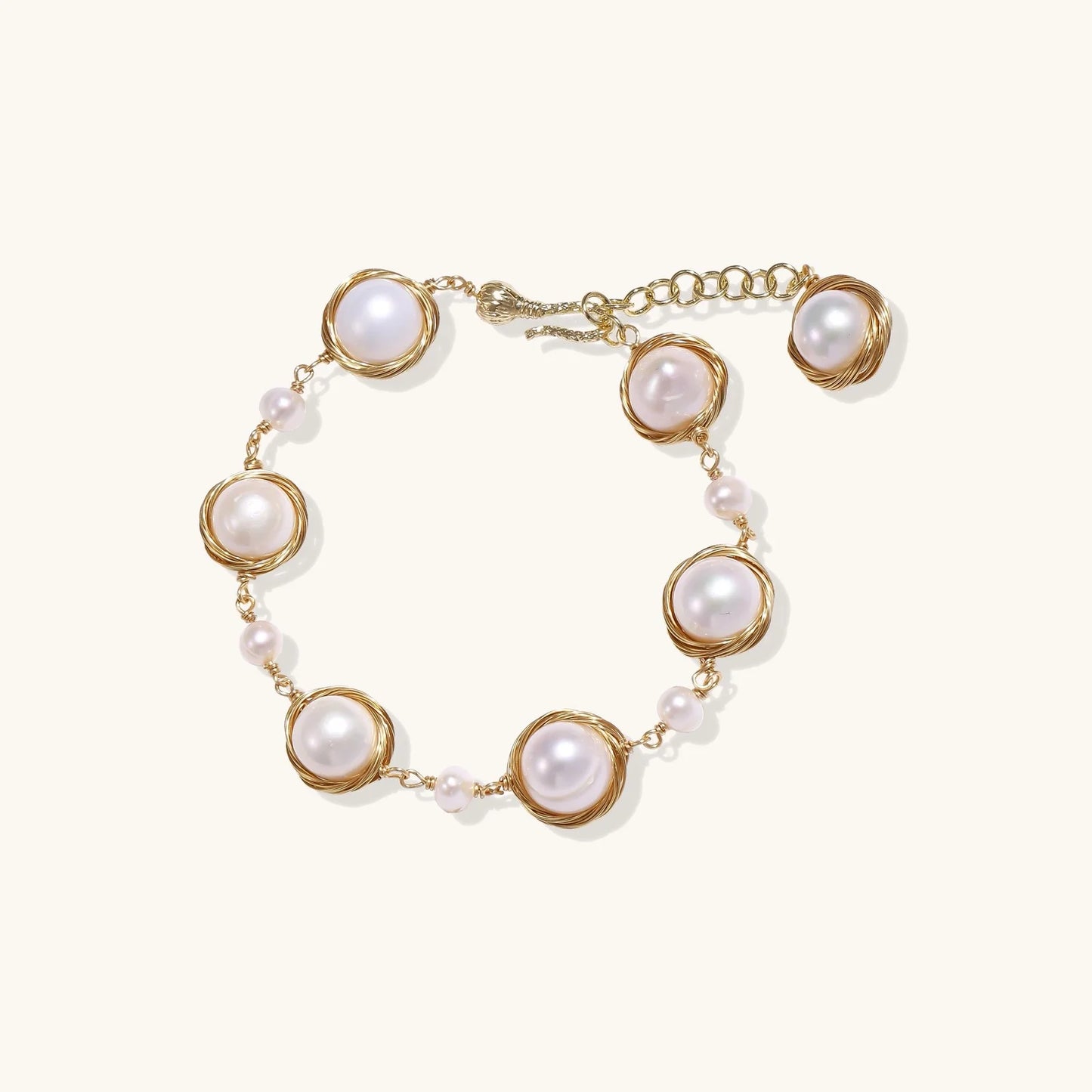 Gold wire-wrapped freshwater pearl bracelet with alternating pearl sizes on cream background, adjustable length
