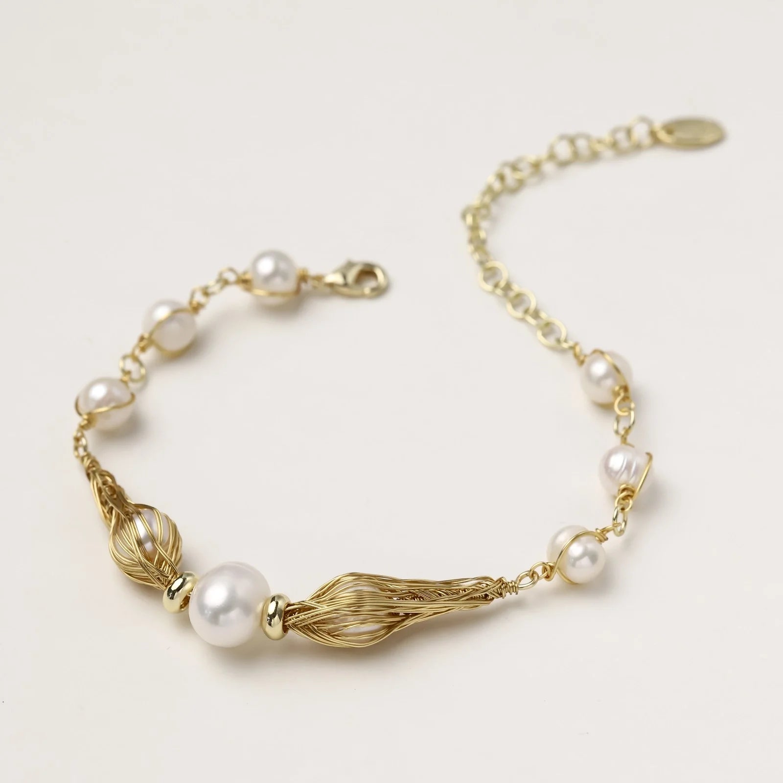 Adjustable gold bracelet with freshwater pearls and textured filigree beads on white background, showing clasp detail.
