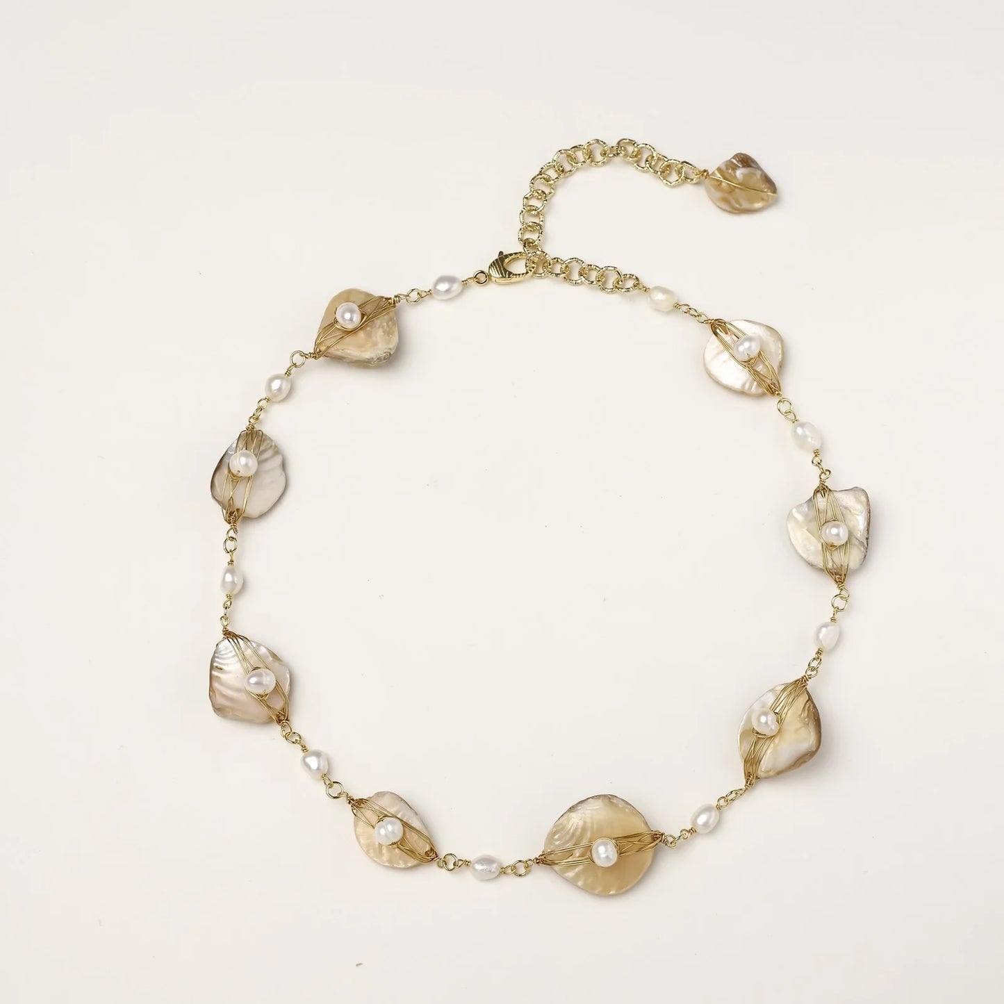Gold-plated necklace with wire-wrapped shell pieces and freshwater pearls on neutral background, adjustable chain visible.