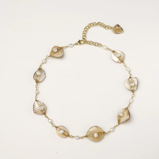 Gold-plated necklace with wire-wrapped shell pieces and freshwater pearls on neutral background, adjustable chain visible.