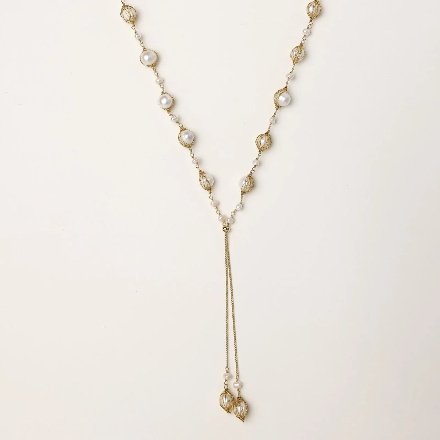 Adjustable gold lariat necklace with freshwater pearls nested in delicate cage settings and Y-shaped tassel drop