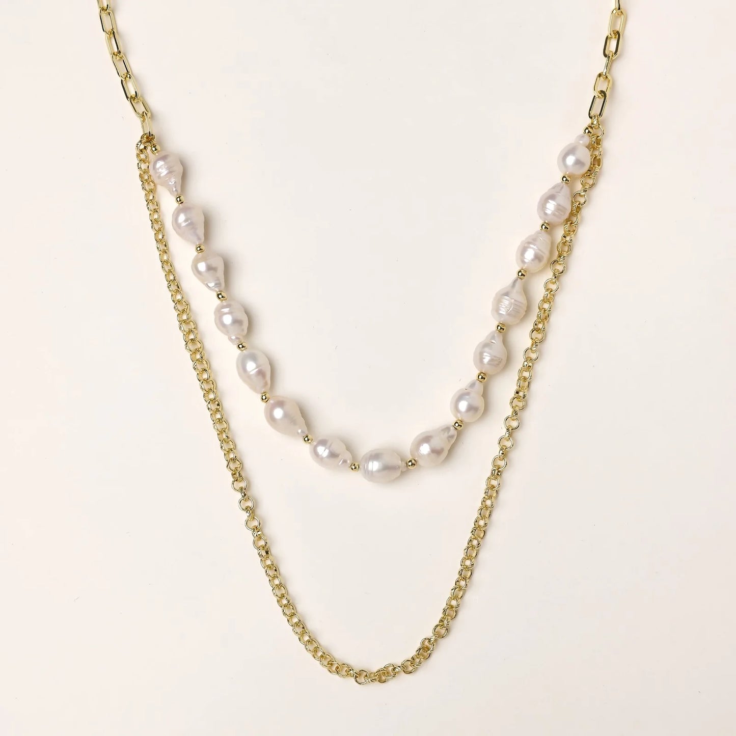 Layered gold chain necklace with organic baroque freshwater pearls and adjustable length on cream background
