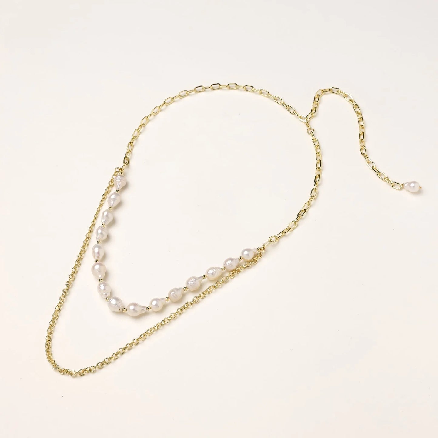 Layered gold chain necklace with organic baroque freshwater pearls and adjustable length on cream background
