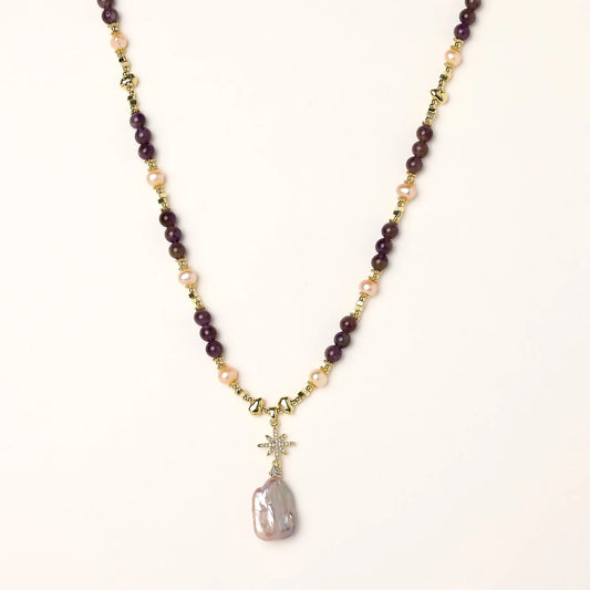 Gold necklace with iridescent baroque pearl pendant, purple amethyst beads, and crystal star charm on cream background