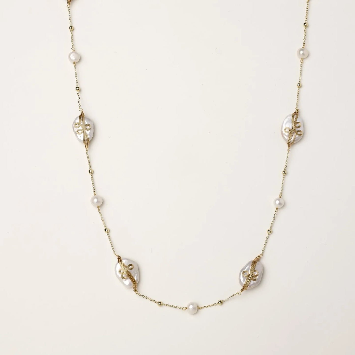 Long gold chain necklace with baroque pearls wrapped in leaf designs and small freshwater pearls spaced along the strand