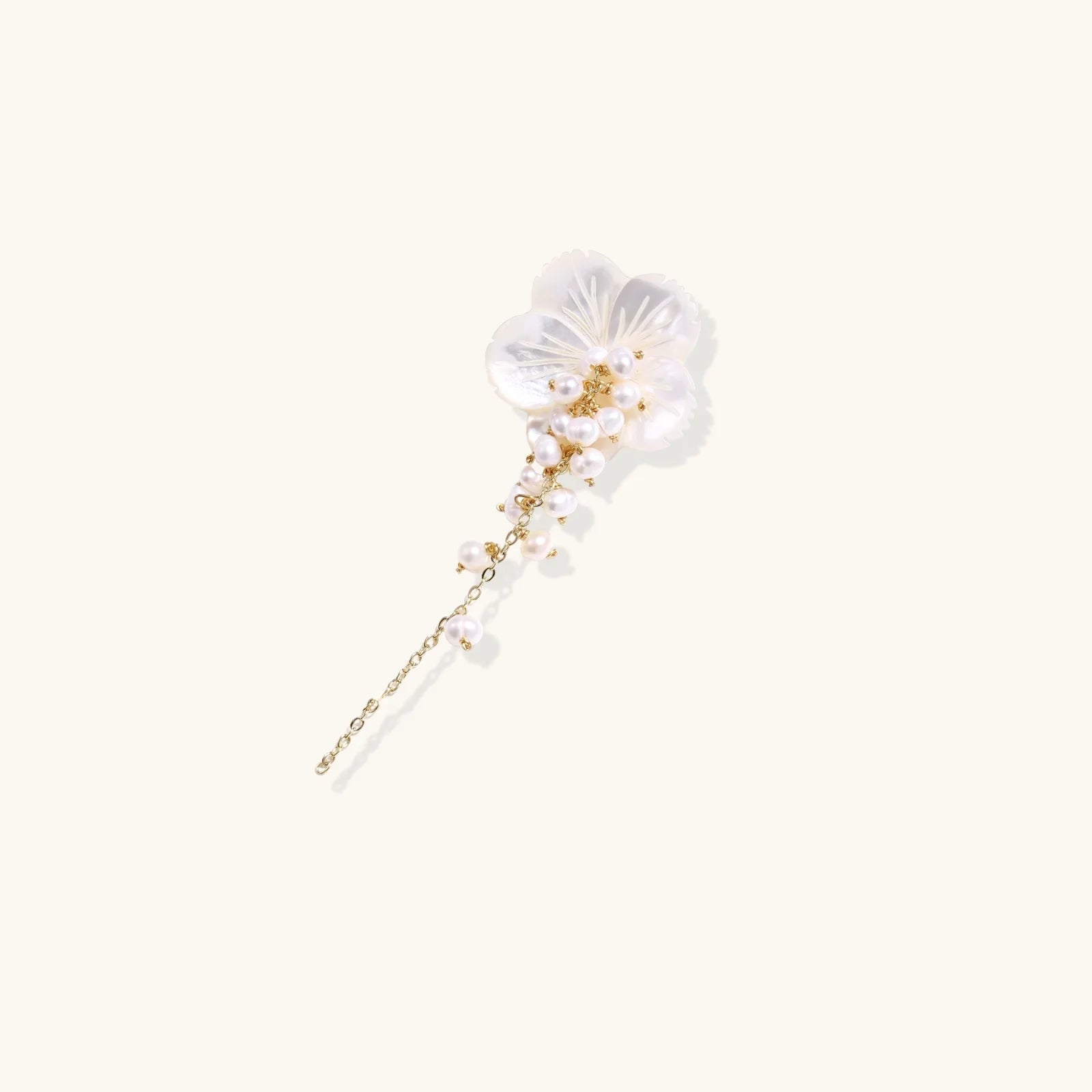Iridescent shell flower brooch with carved petals and cascading freshwater pearls on gold chain against cream background.