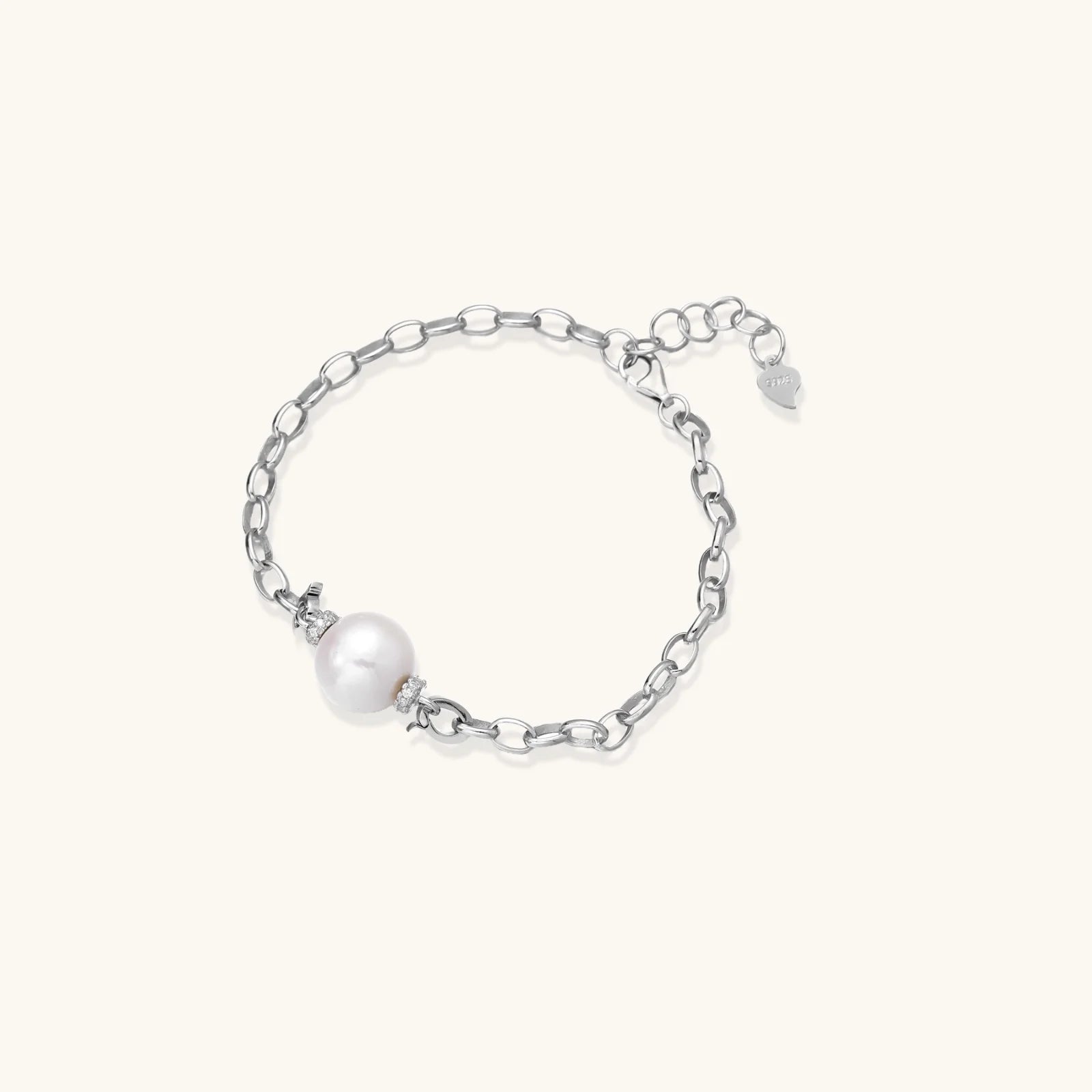 Rhodium-plated silver chain bracelet with single white freshwater pearl and heart charm clasp on cream background