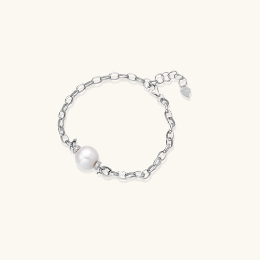 Rhodium-plated silver chain bracelet with single white freshwater pearl and heart charm clasp on cream background