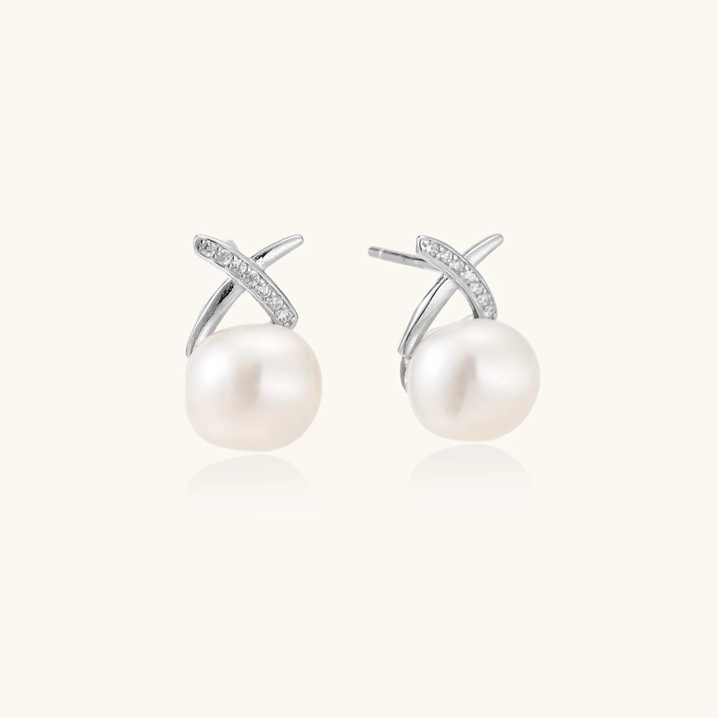 Rhodium-plated silver stud earrings with sparkling X design above lustrous round freshwater pearls on white background.