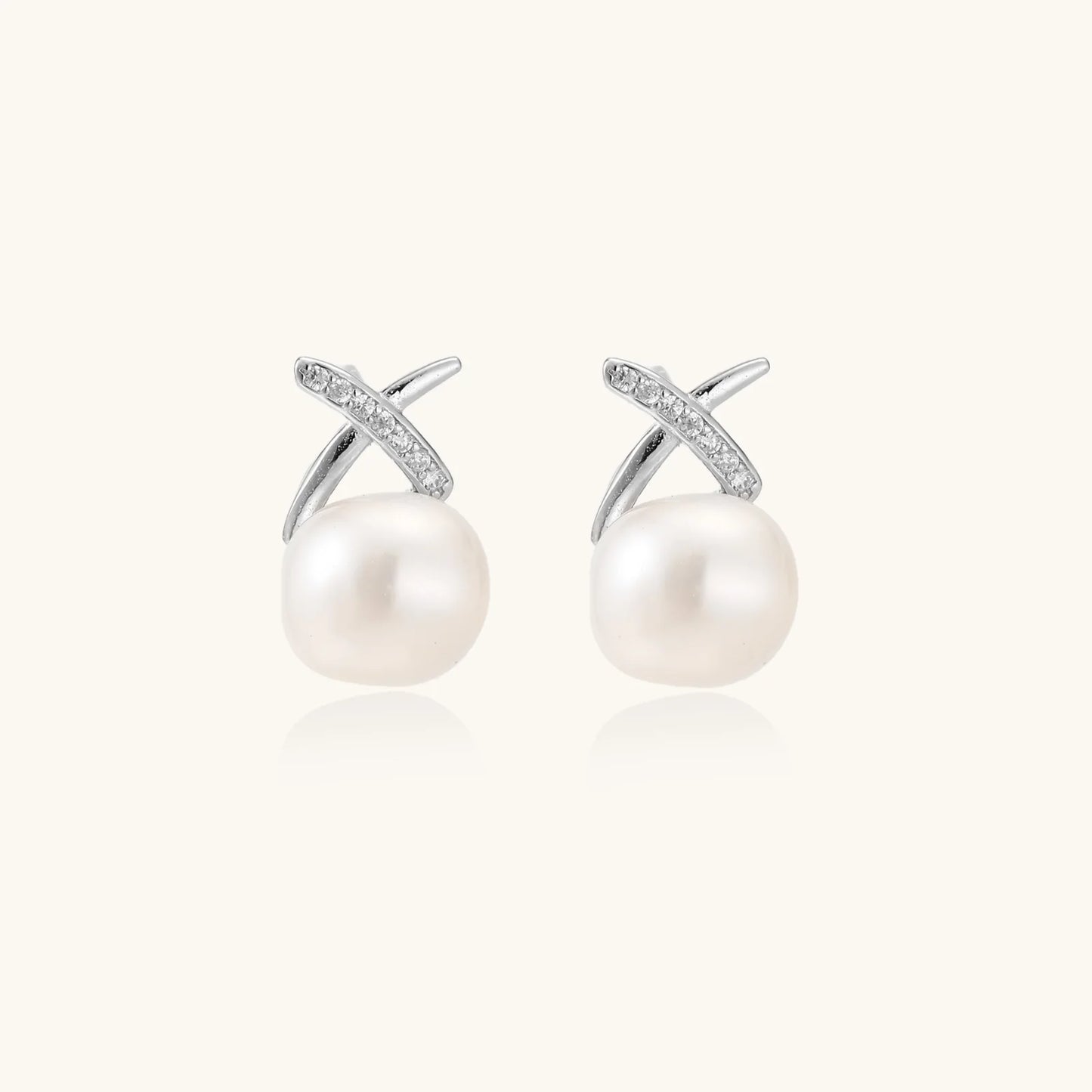 Rhodium-plated silver stud earrings with sparkling X design above lustrous round freshwater pearls on white background.