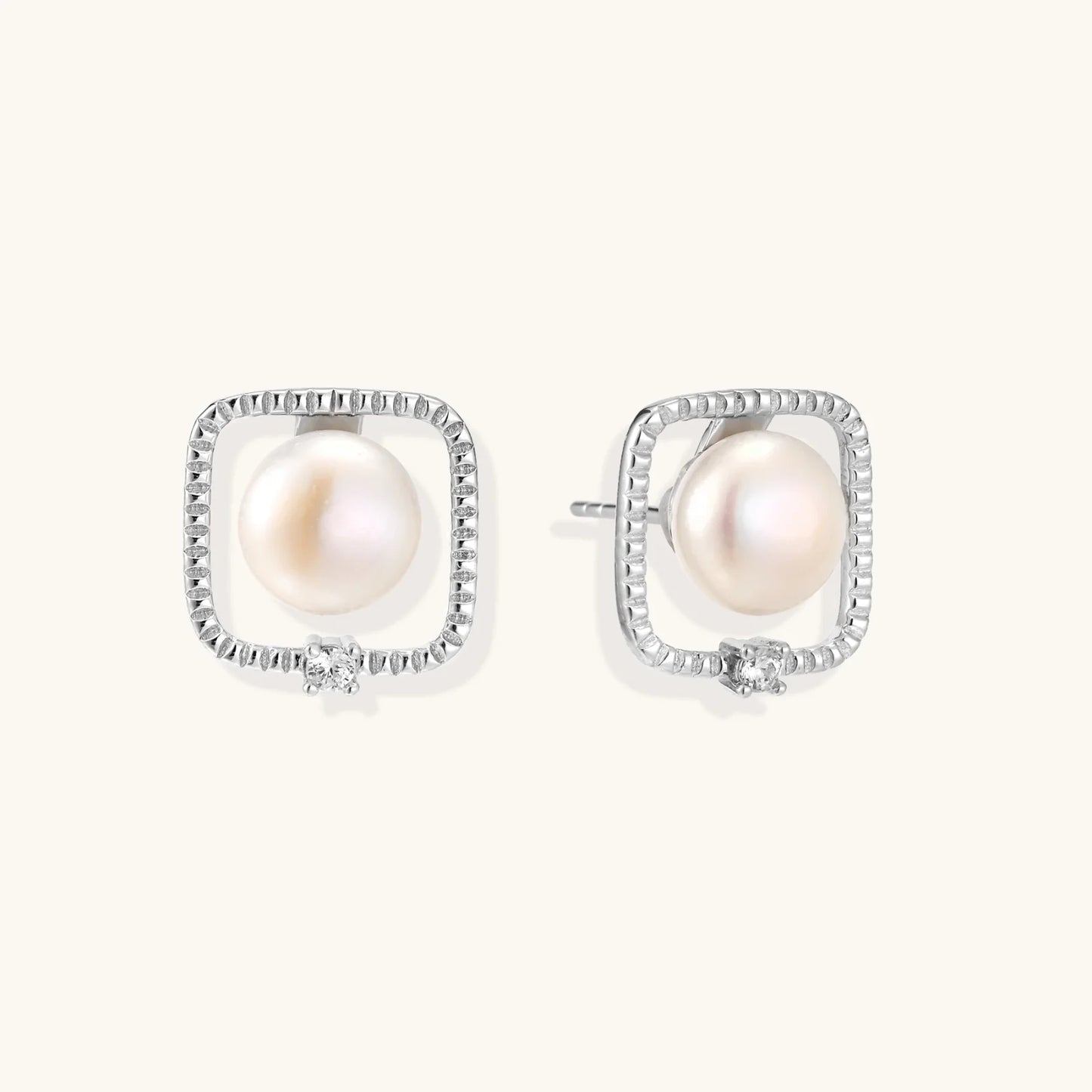 Rhodium-plated silver stud earrings with cushion frame, centered freshwater pearl, and tiny crystal accent