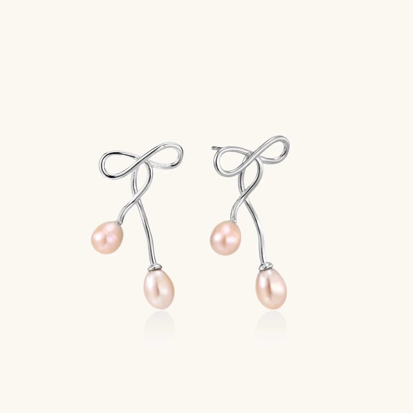Rhodium-plated silver earrings with organic vine curves and two peachy freshwater pearls on cream background