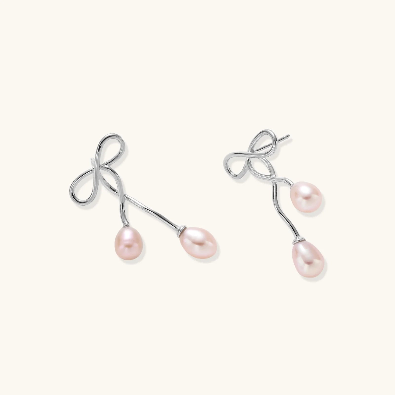 Rhodium-plated silver earrings with organic vine curves and two peachy freshwater pearls on cream background
