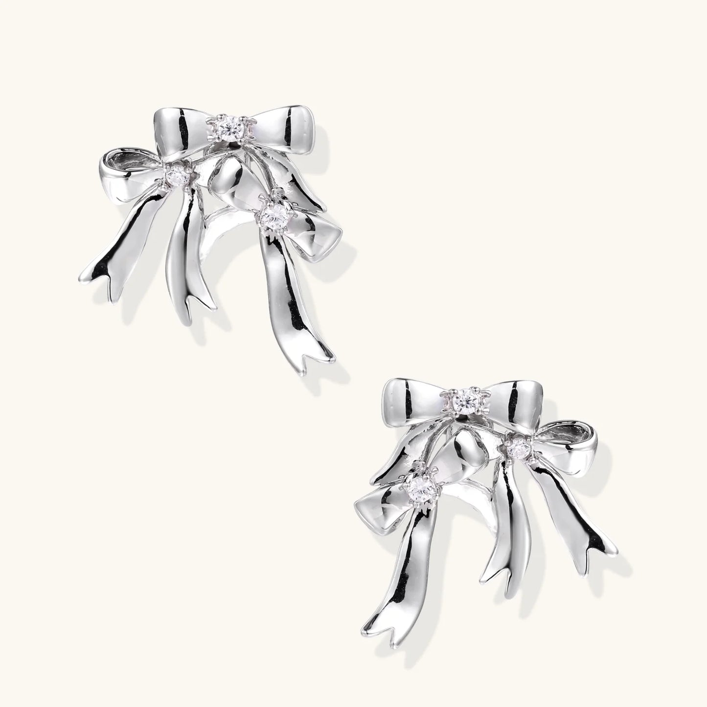 Sculptural bow earrings in polished white gold plate with sparkling zirconia stones and flowing ribbon details