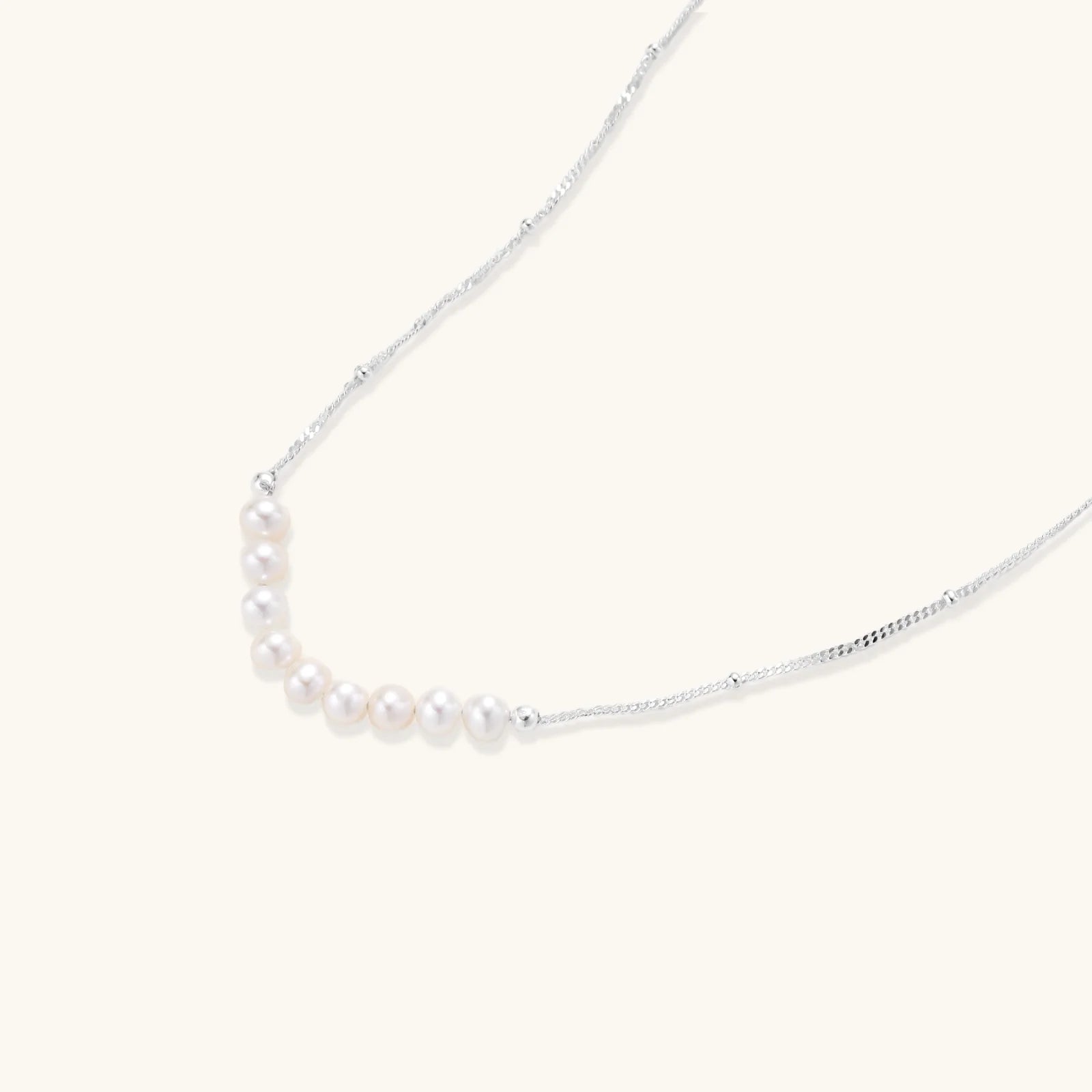 Delicate sterling silver chain necklace with small freshwater pearls arranged in a curved smile arc on cream background.