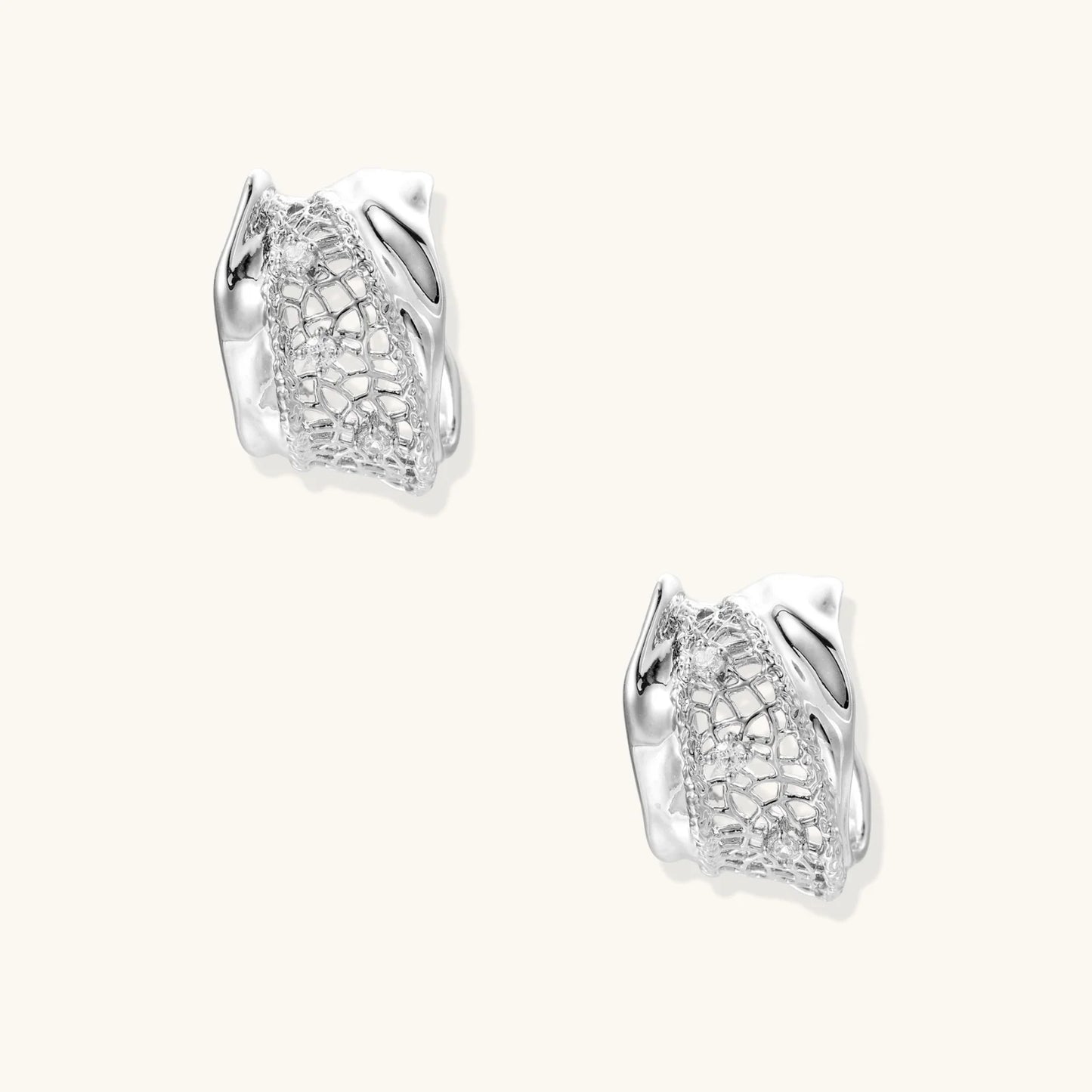 Close-up of sculptural hoop earrings with lattice center band and smooth twisted edges in white gold-plated brass with zirconia