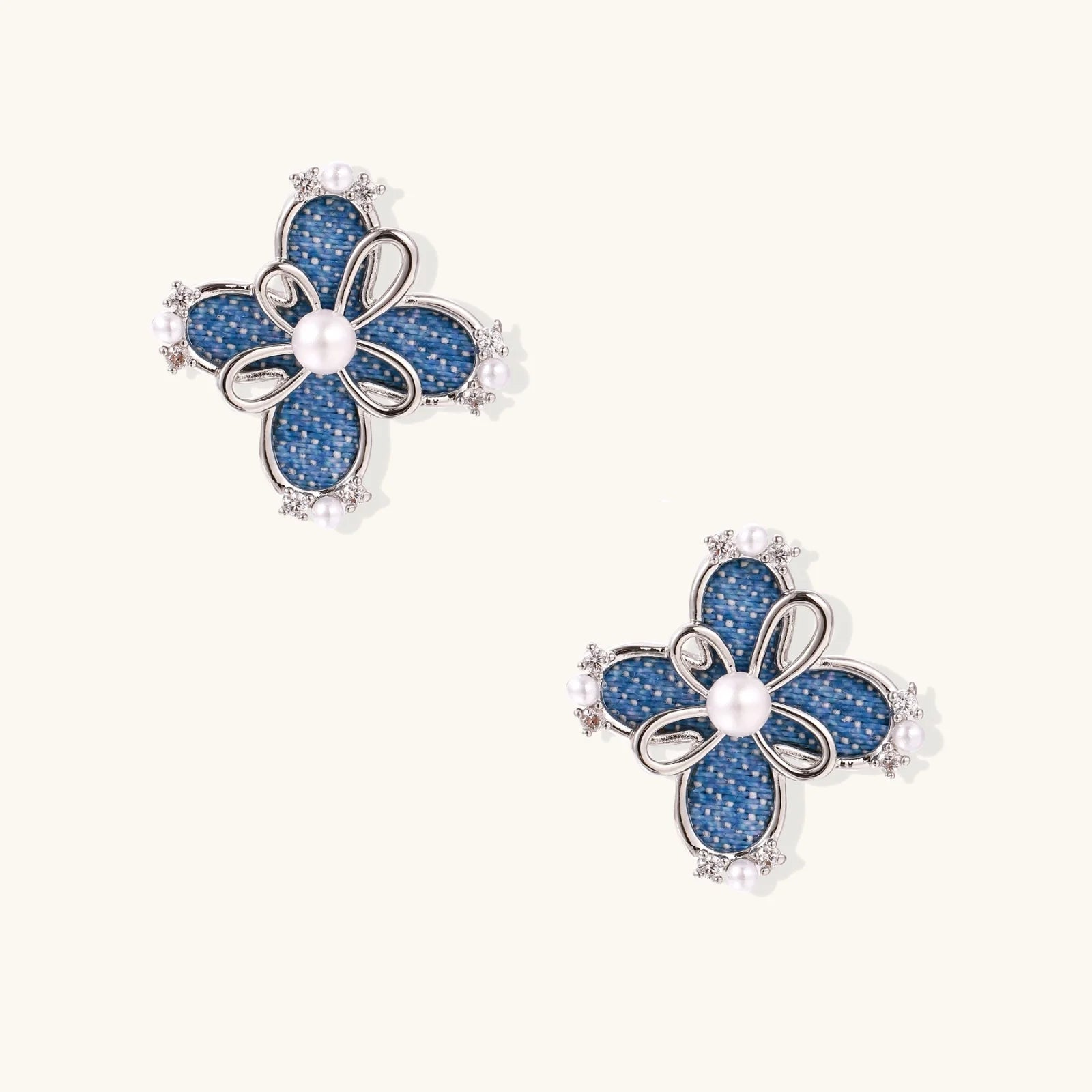 Blue denim fabric flower studs with white gold plated petals, pearl center, and zirconia accents on white background