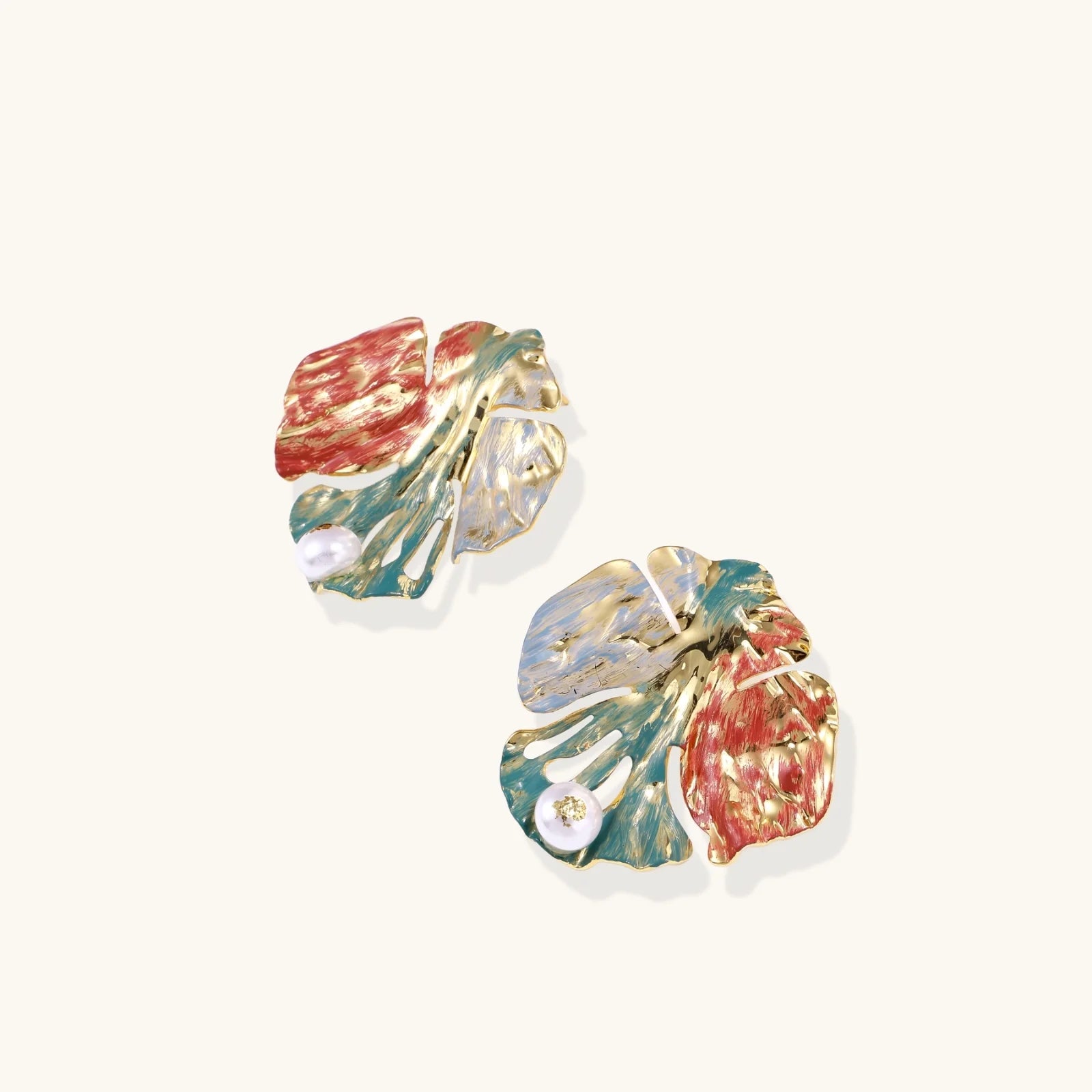 Artistic monstera-shaped earrings with teal, coral, and cream enamel brushstrokes, gold trim, and white pearl accent