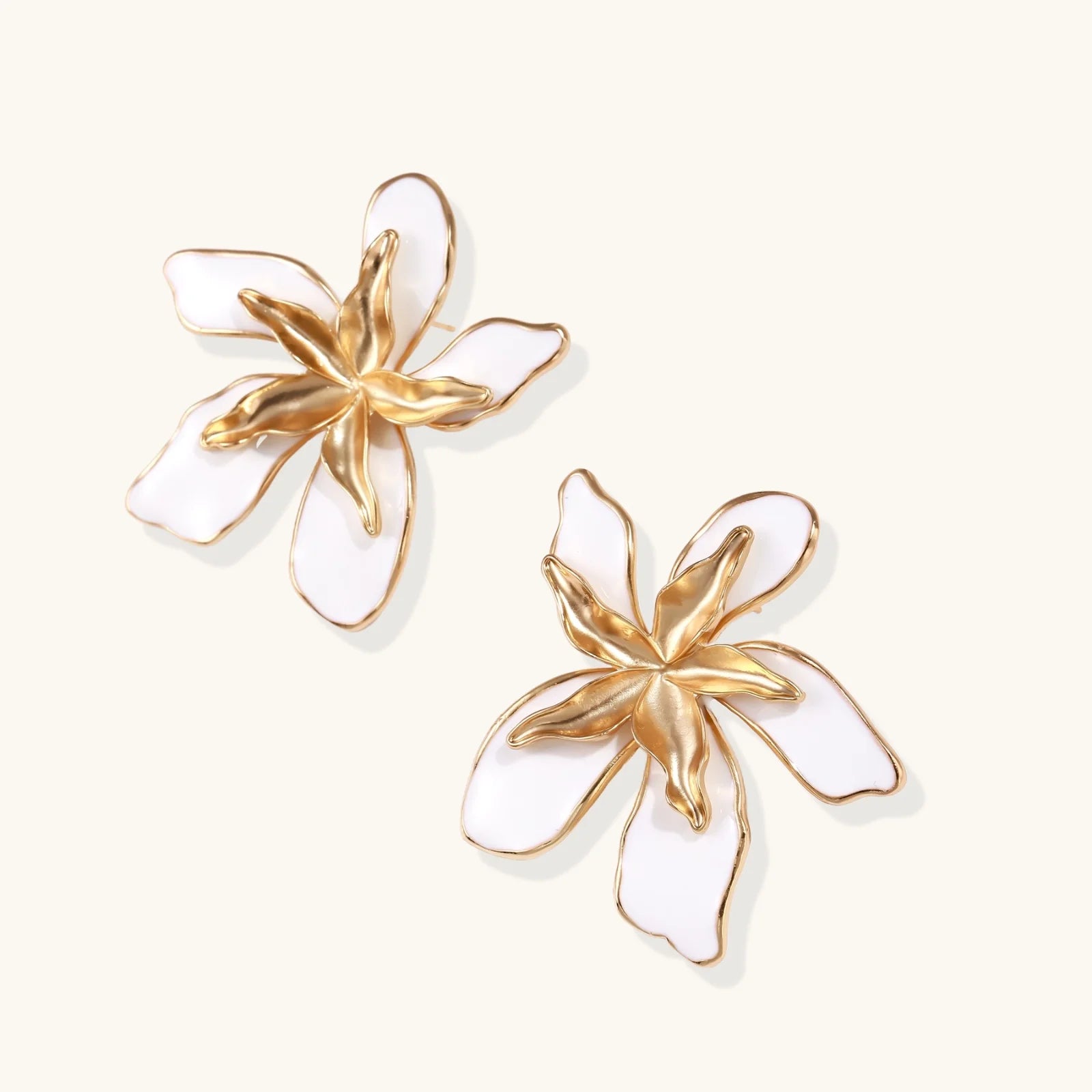 White enamel tropical flower earrings with sculptural gold-plated center and organic petal design on cream background