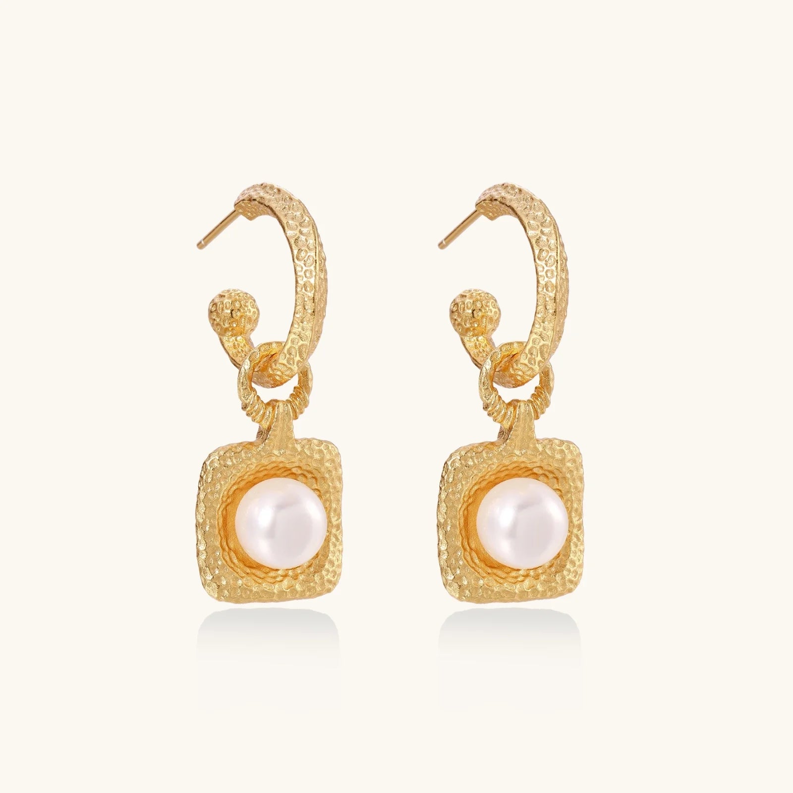 Pair of gold vermeil hoop earrings with textured square frames holding freshwater pearls on cream background