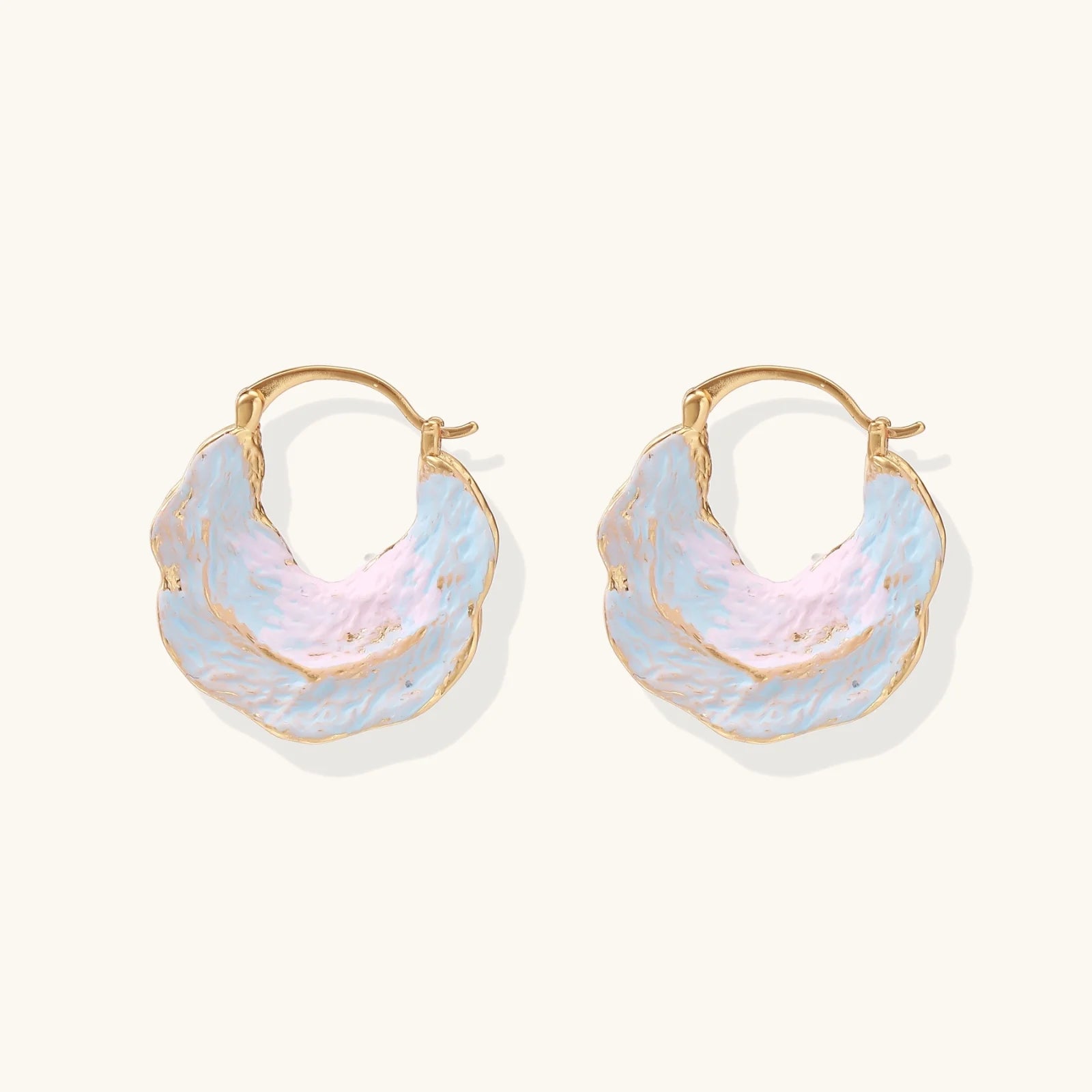 Shell-shaped hoop earrings with iridescent blue-pink enamel and gold trim on cream background