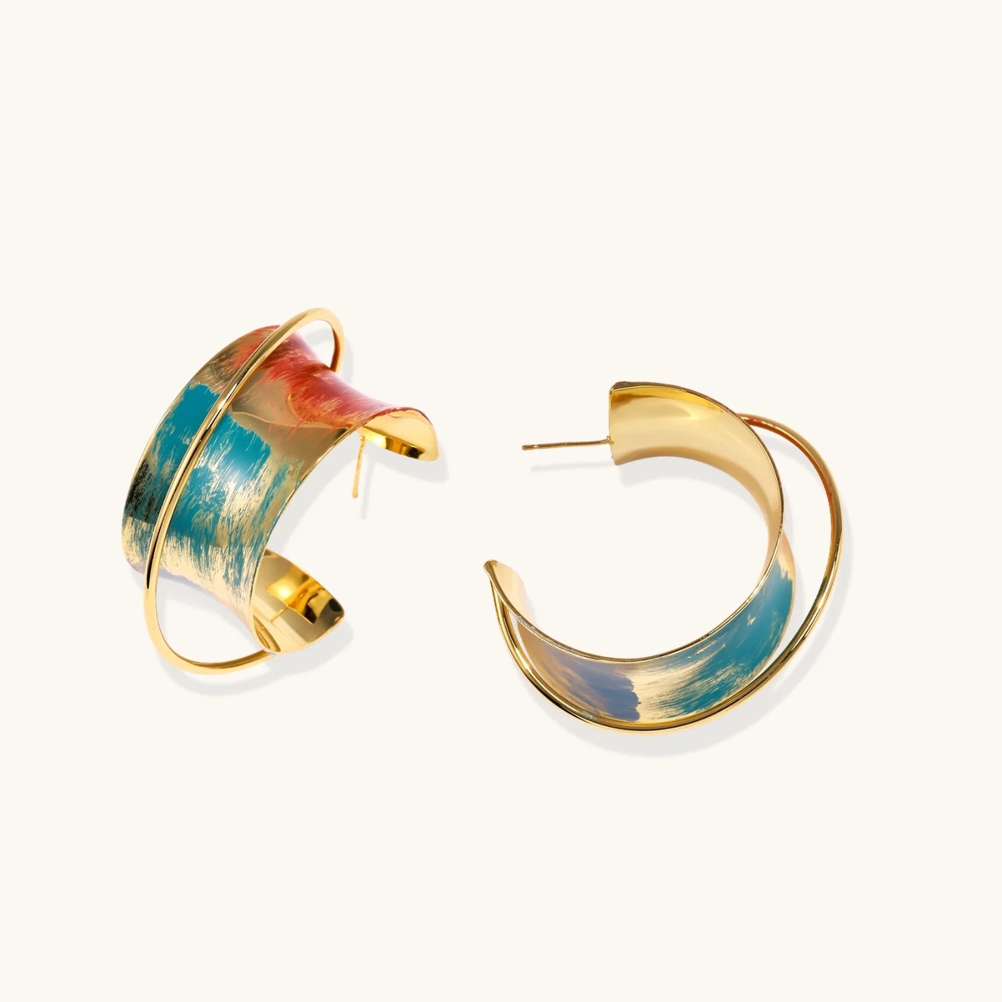 Gold-plated hoop earrings with teal and coral enamel brushstroke design on cream background