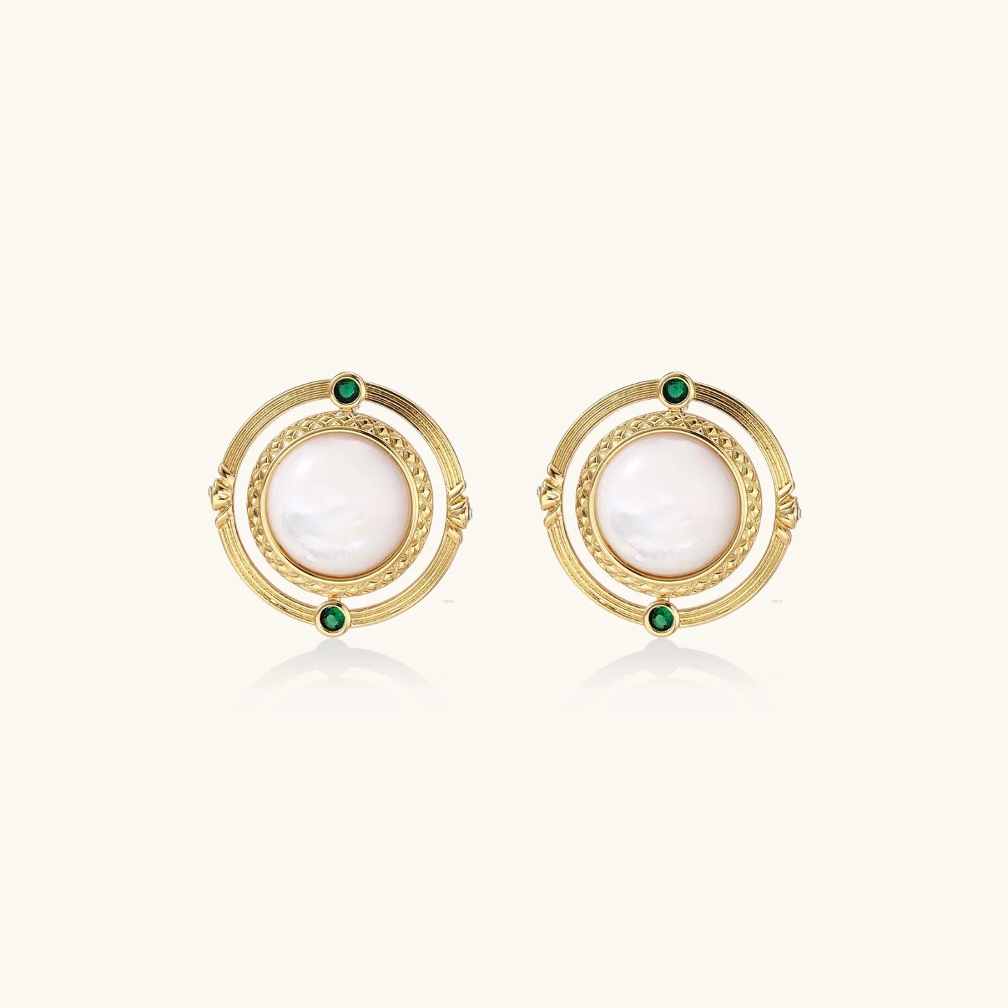 Circular gold stud earrings with iridescent mother-of-pearl center and green zirconia accents on cream background.