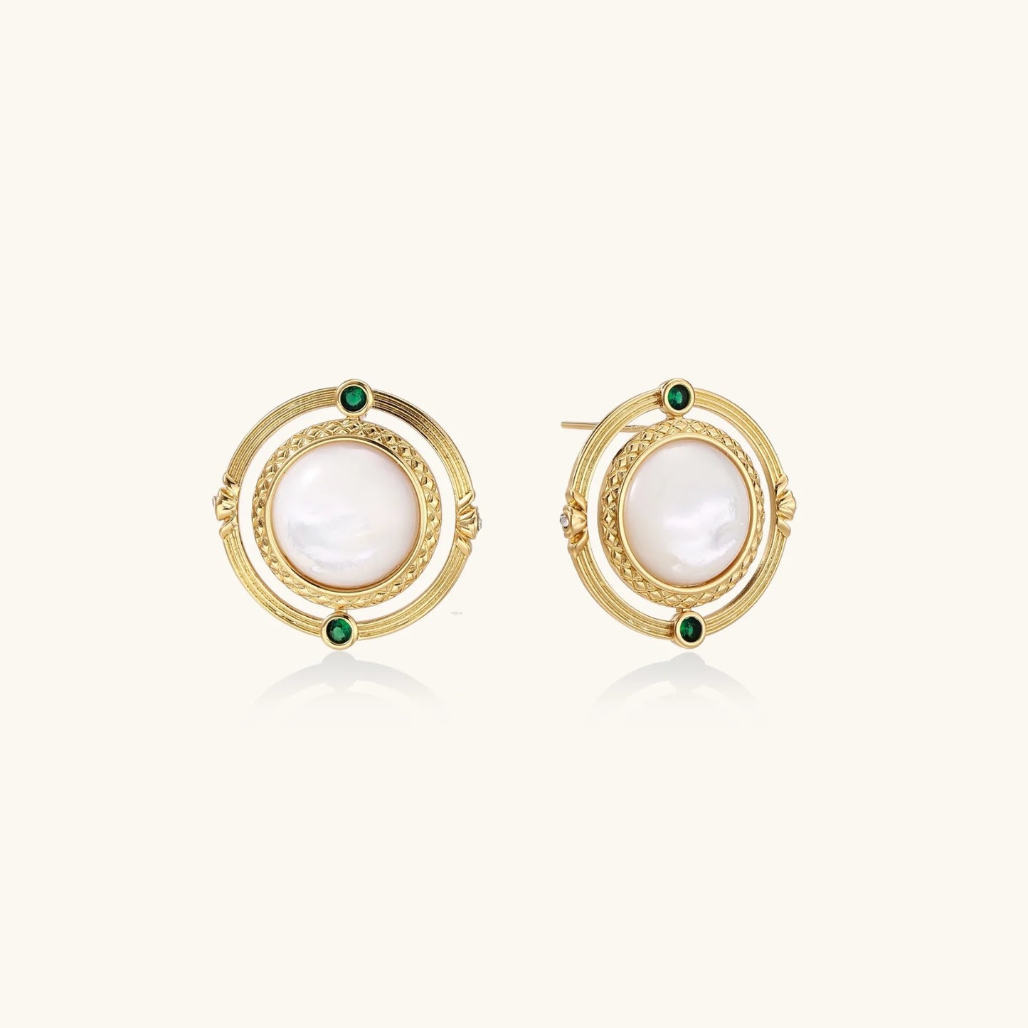 Circular gold stud earrings with iridescent mother-of-pearl center and green zirconia accents on cream background.