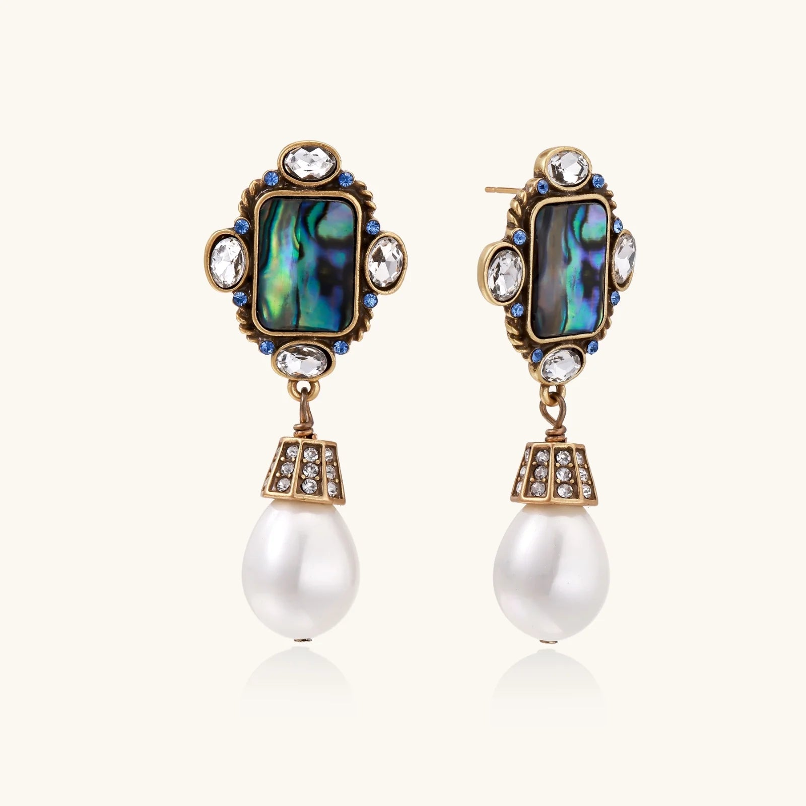 Ornate gold-plated earrings with iridescent abalone shell, crystals, blue stones, and white pearl drops on cream background.
