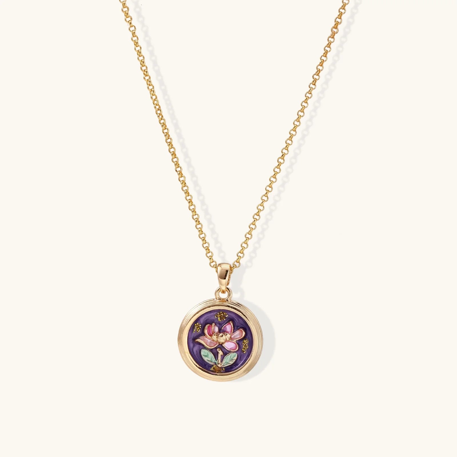 Gold-plated circular pendant with hand-painted purple enamel floral design on delicate chain against cream background