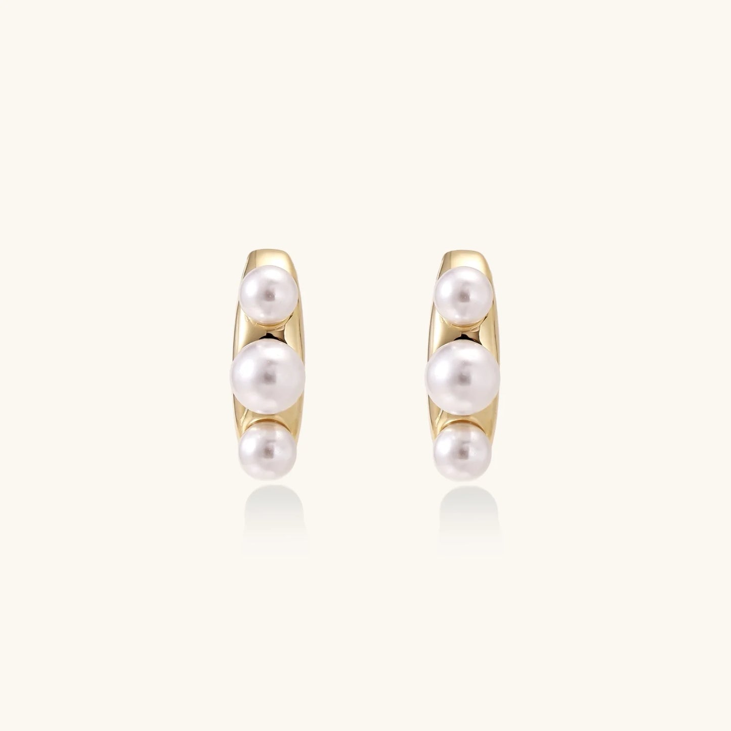 14K gold-plated curved stud earrings with three white freshwater pearls aligned vertically on cream background