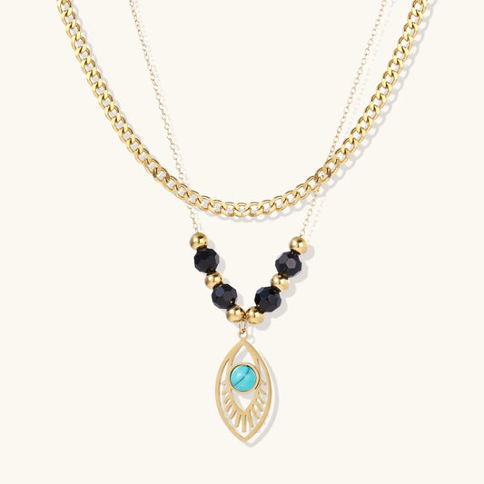 Layered gold necklace with turquoise evil eye pendant and black quartz beads on cream background