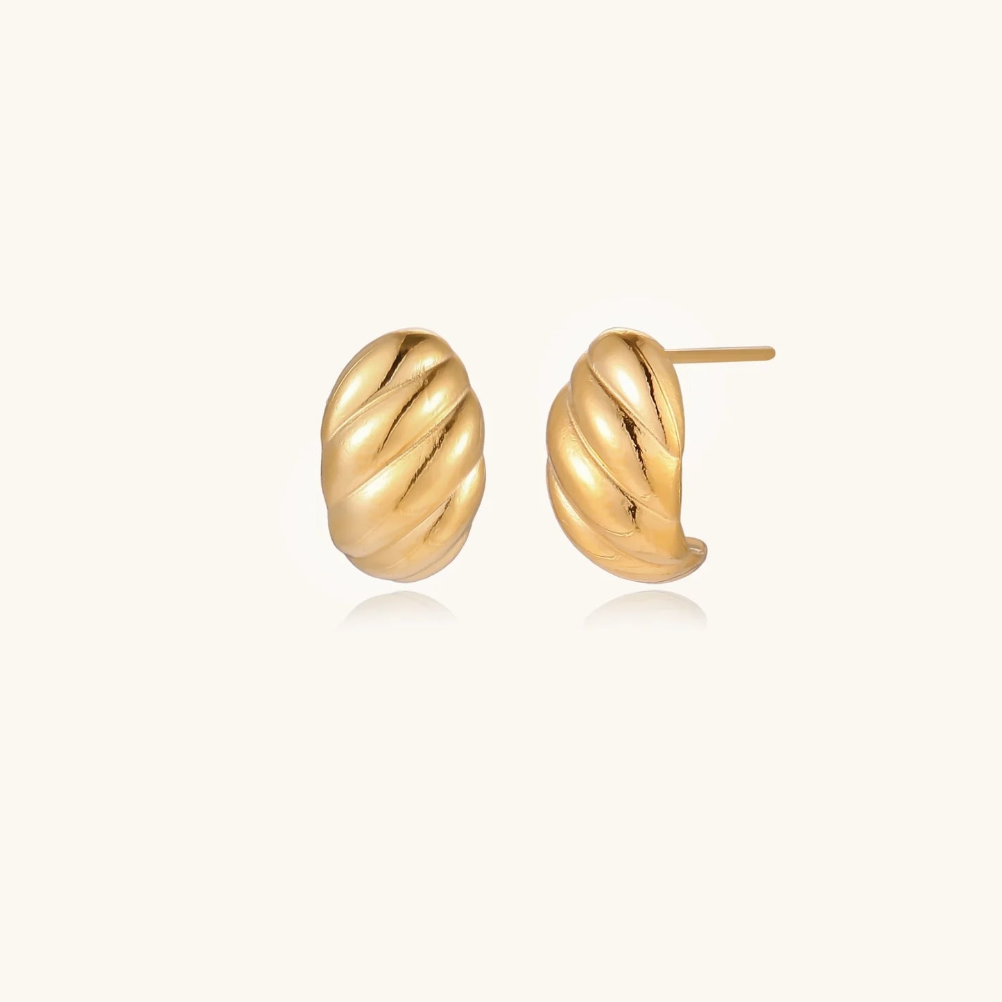 Chunky gold twisted rope huggie hoops with diagonal grooves and high-polish finish on cream background
