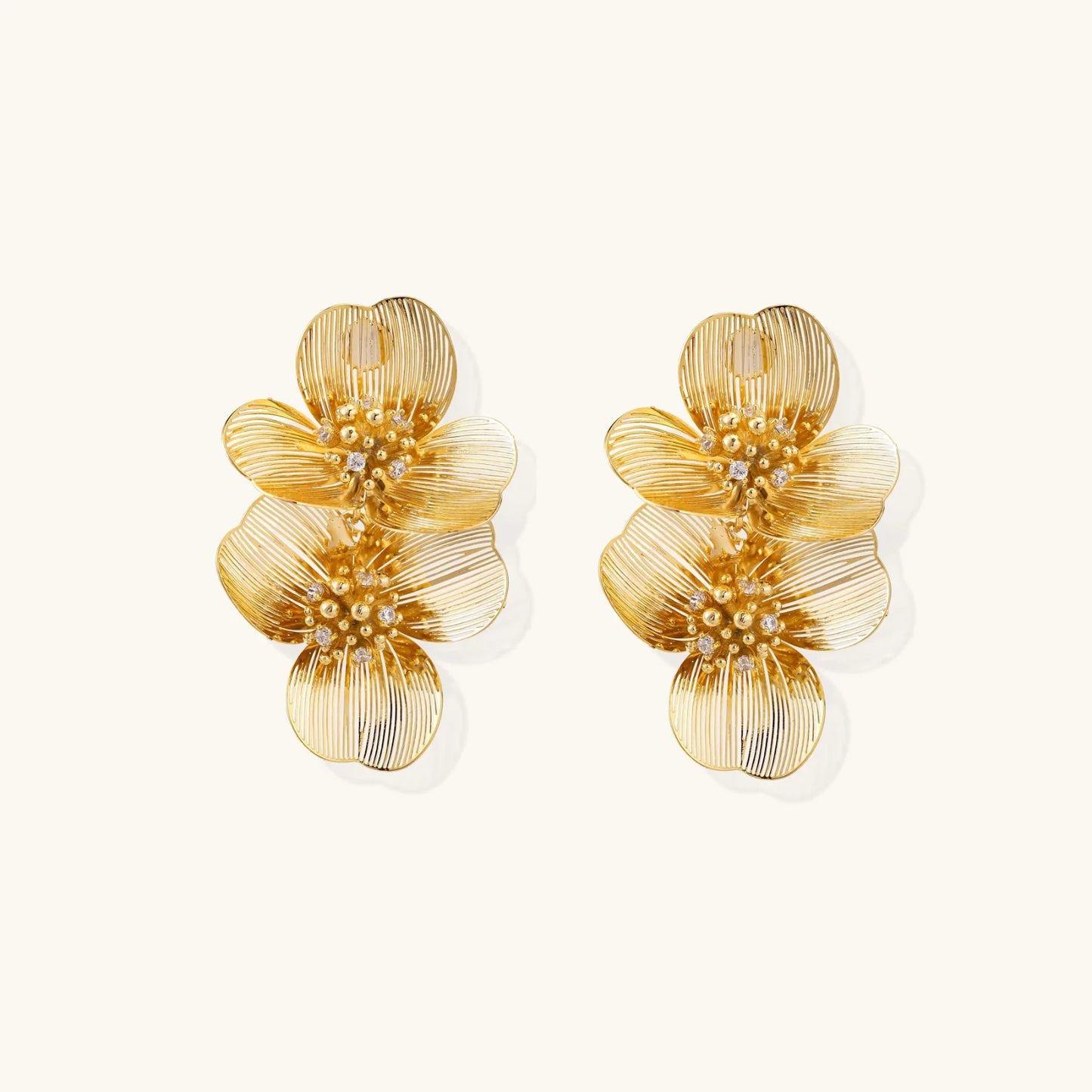 Pair of gold-plated double flower earrings with textured petals and crystal centers on cream background.