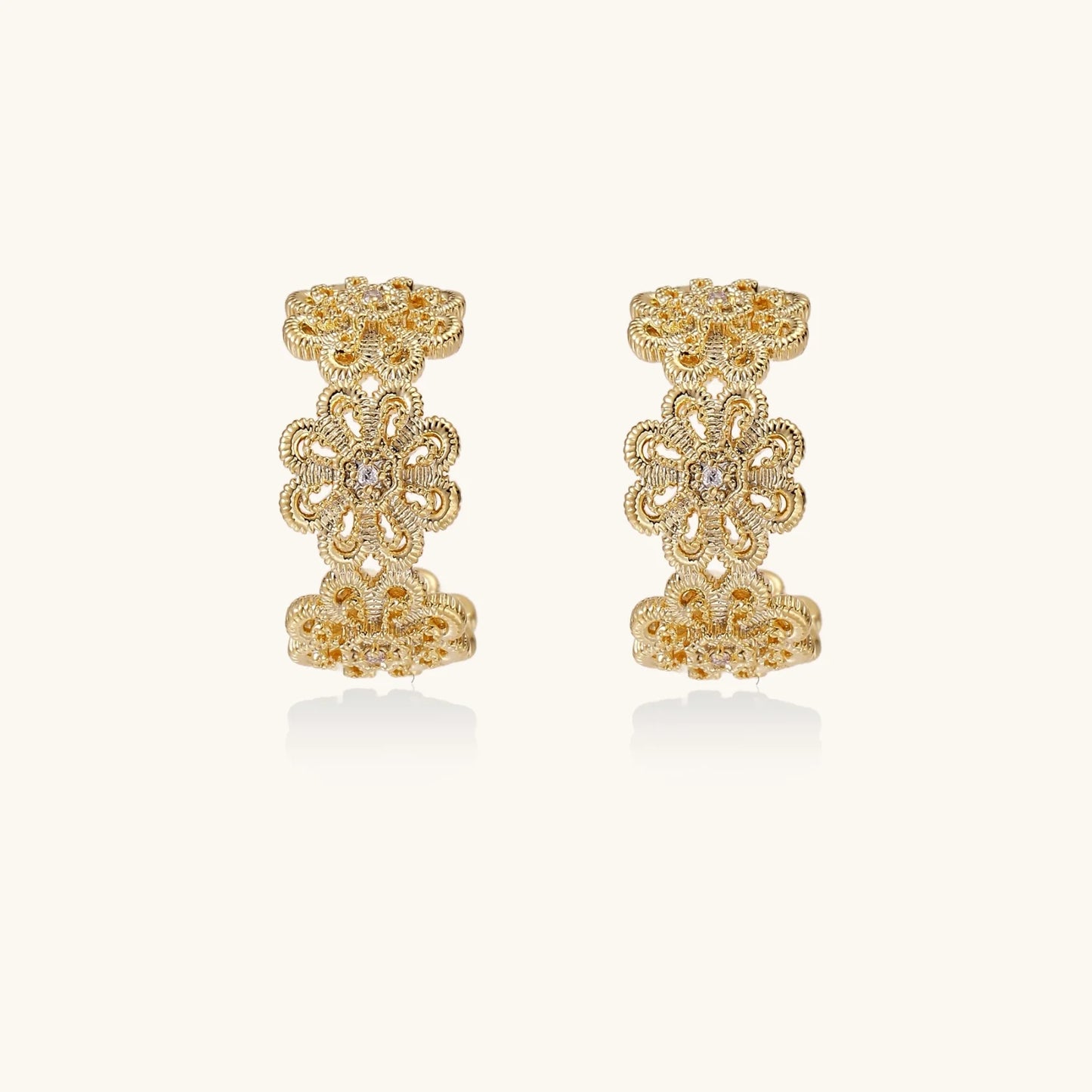 Gold hoop earrings with intricate three-dimensional floral filigree pattern in 14K gold plated brass on cream background