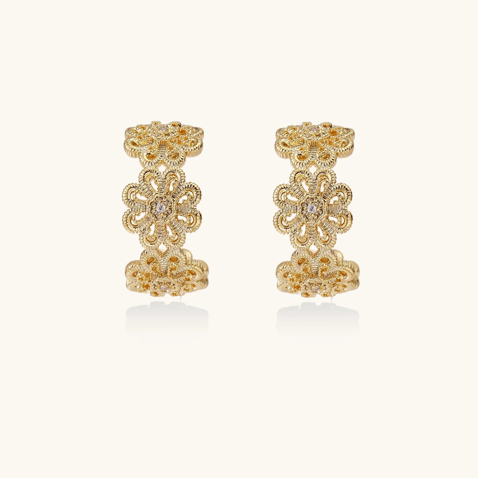 Gold hoop earrings with intricate three-dimensional floral filigree pattern in 14K gold plated brass on cream background