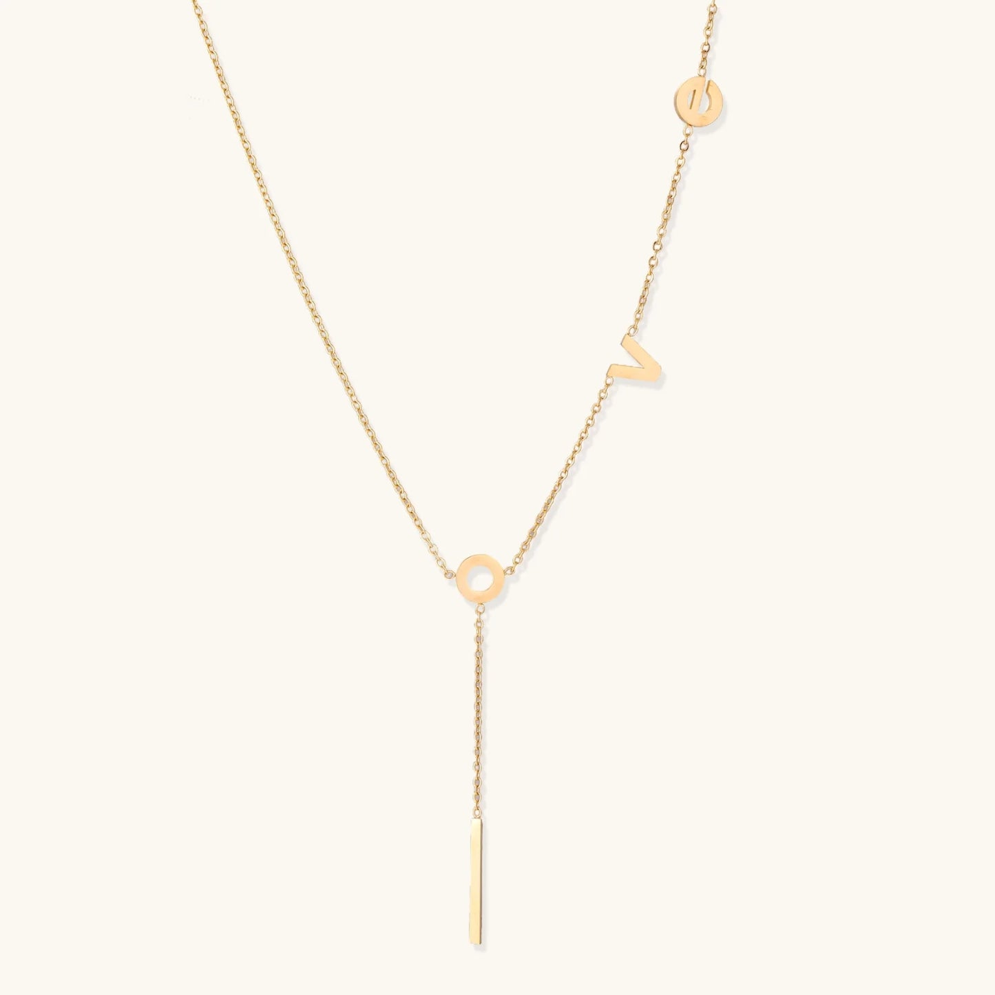 Gold Y-shaped necklace with L-O-V-E letter charms and vertical bar pendant on delicate chain against cream background