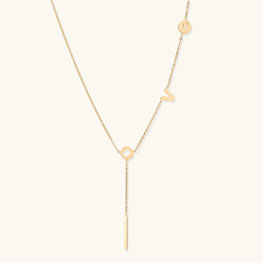 Gold Y-shaped necklace with L-O-V-E letter charms and vertical bar pendant on delicate chain against cream background