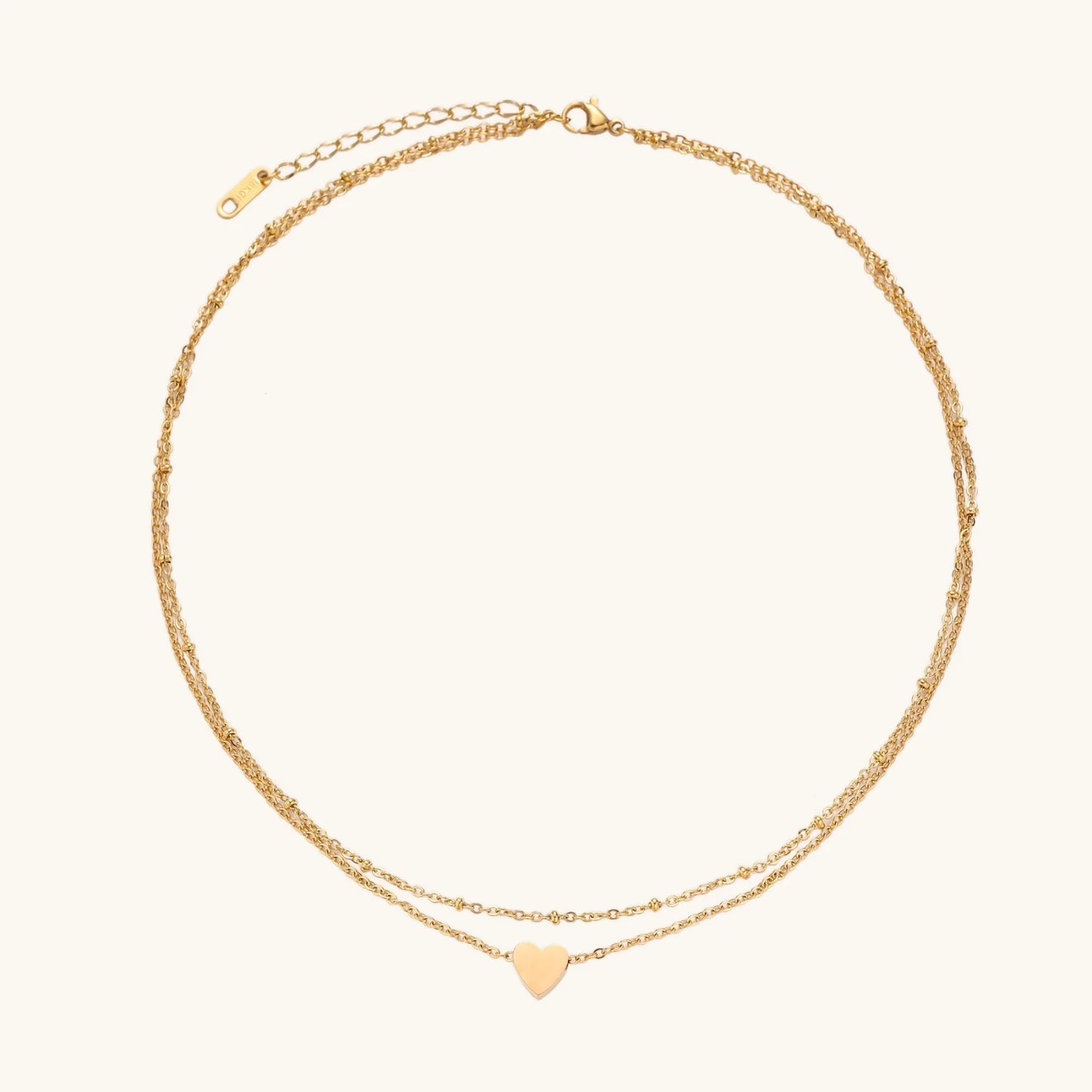 Delicate double-chain gold necklace with tiny heart pendant on cream background