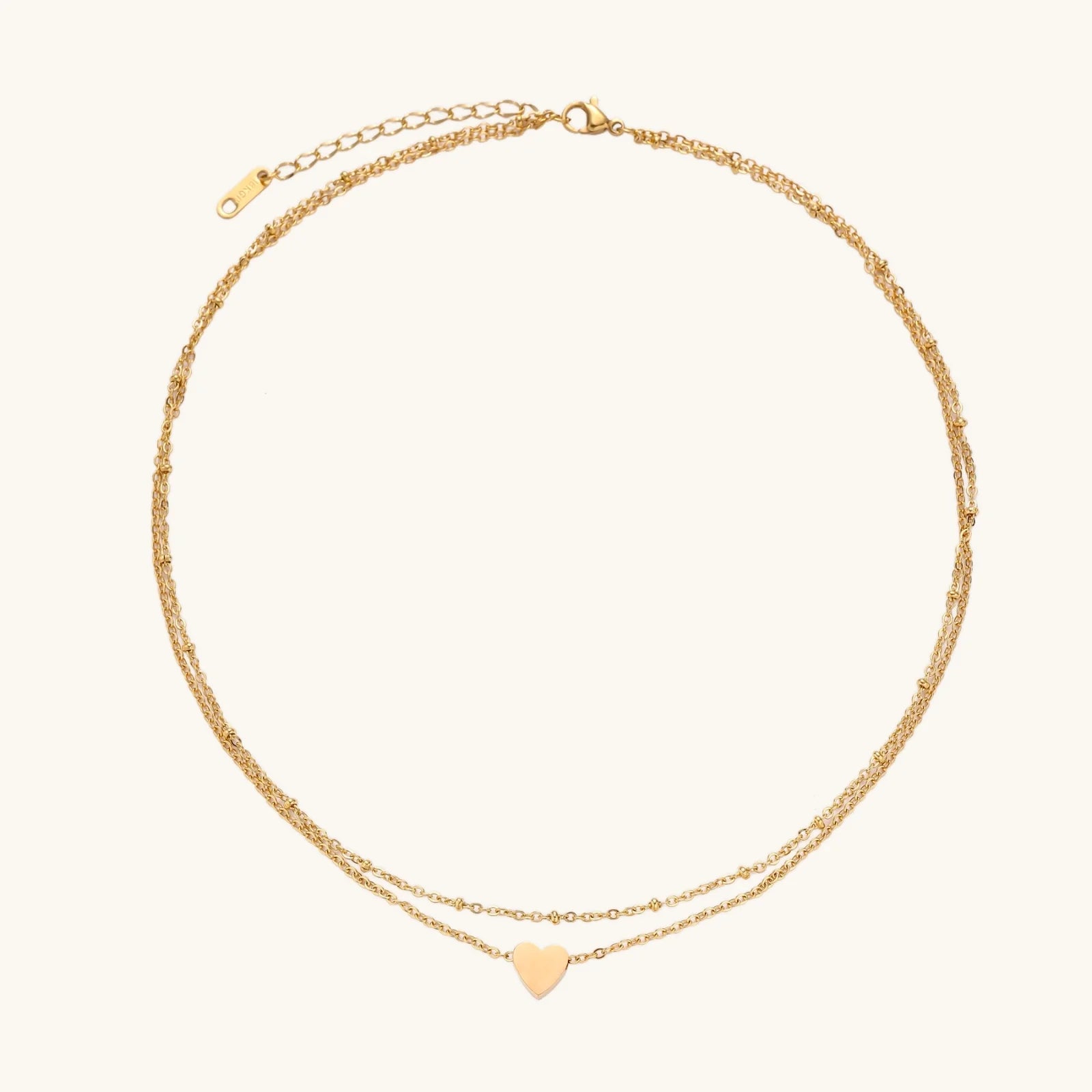 Delicate double-chain gold necklace with tiny heart pendant on cream background