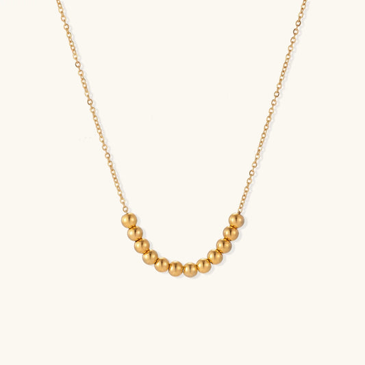 Delicate gold-plated necklace with graduated spherical beads forming gentle smile curve on beige background