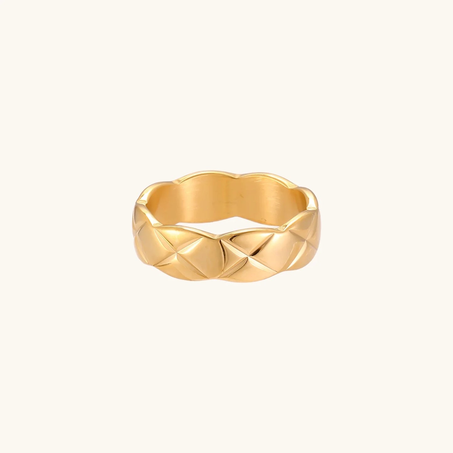 Close-up of an 18K gold-plated twisted band ring with dimensional braided pattern on cream background.