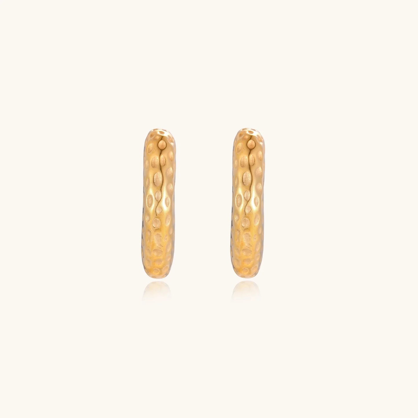 Gold-toned hoop earrings with hammered dimpled texture and post closure on cream background