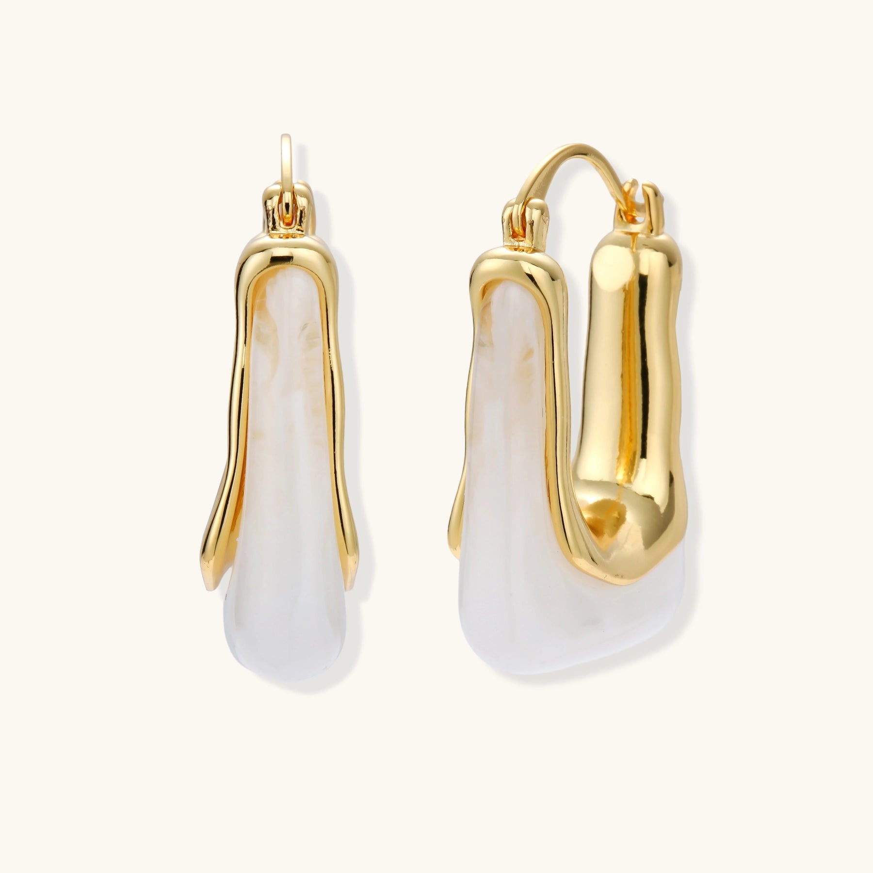 Sculptural gold-plated hoop earrings with flowing curved design and lever-back closure on cream background.