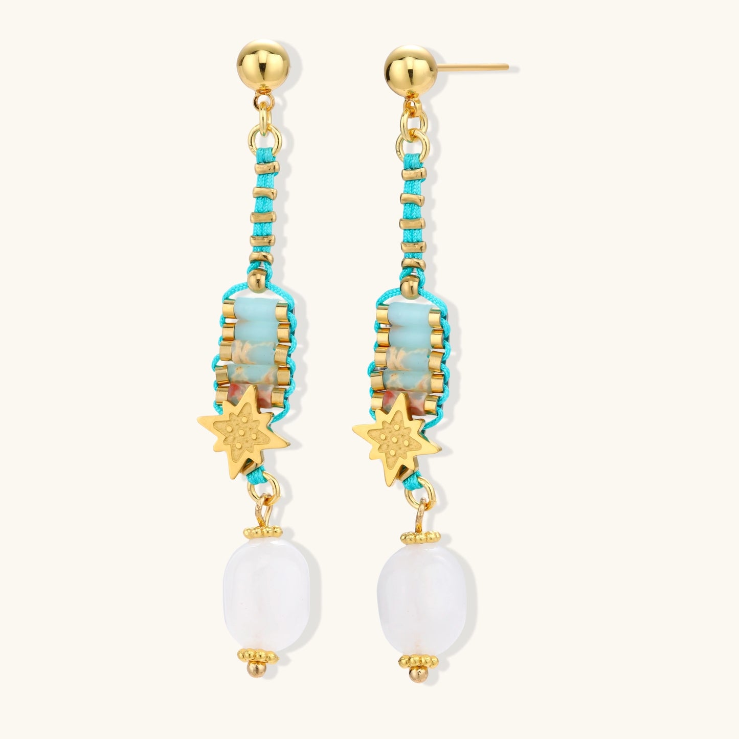 Gold-plated dangle earrings with turquoise threading, star charms, and white pearl beads against cream background.