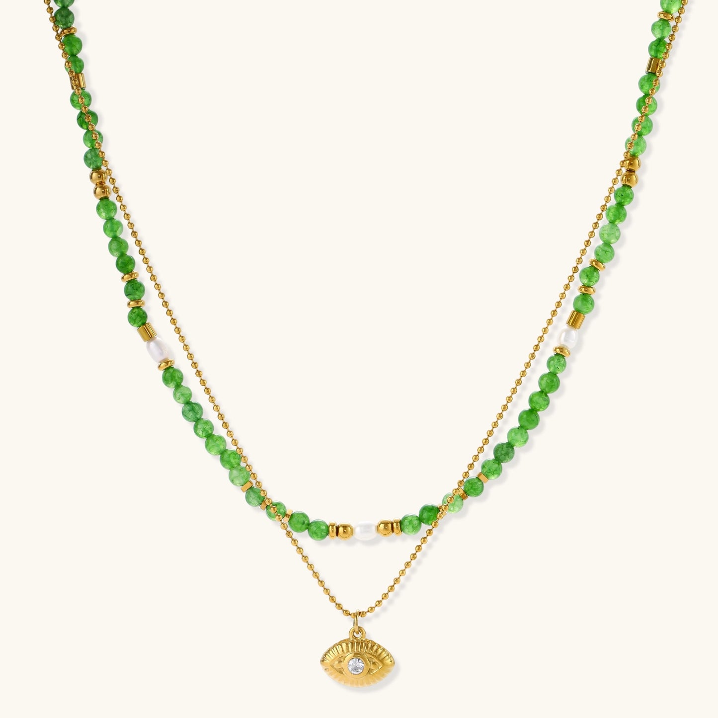 Layered necklace with green stone beads, gold spacers, white accents, and protective eye pendant on cream background.