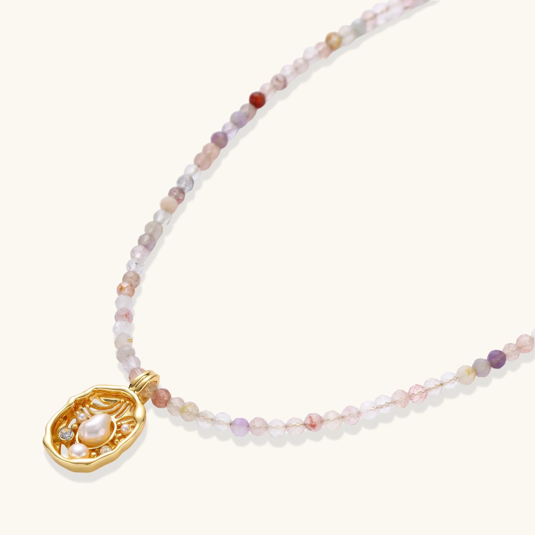 Delicate gold-plated necklace with mixed gemstone beads and ornate oval pendant on white background